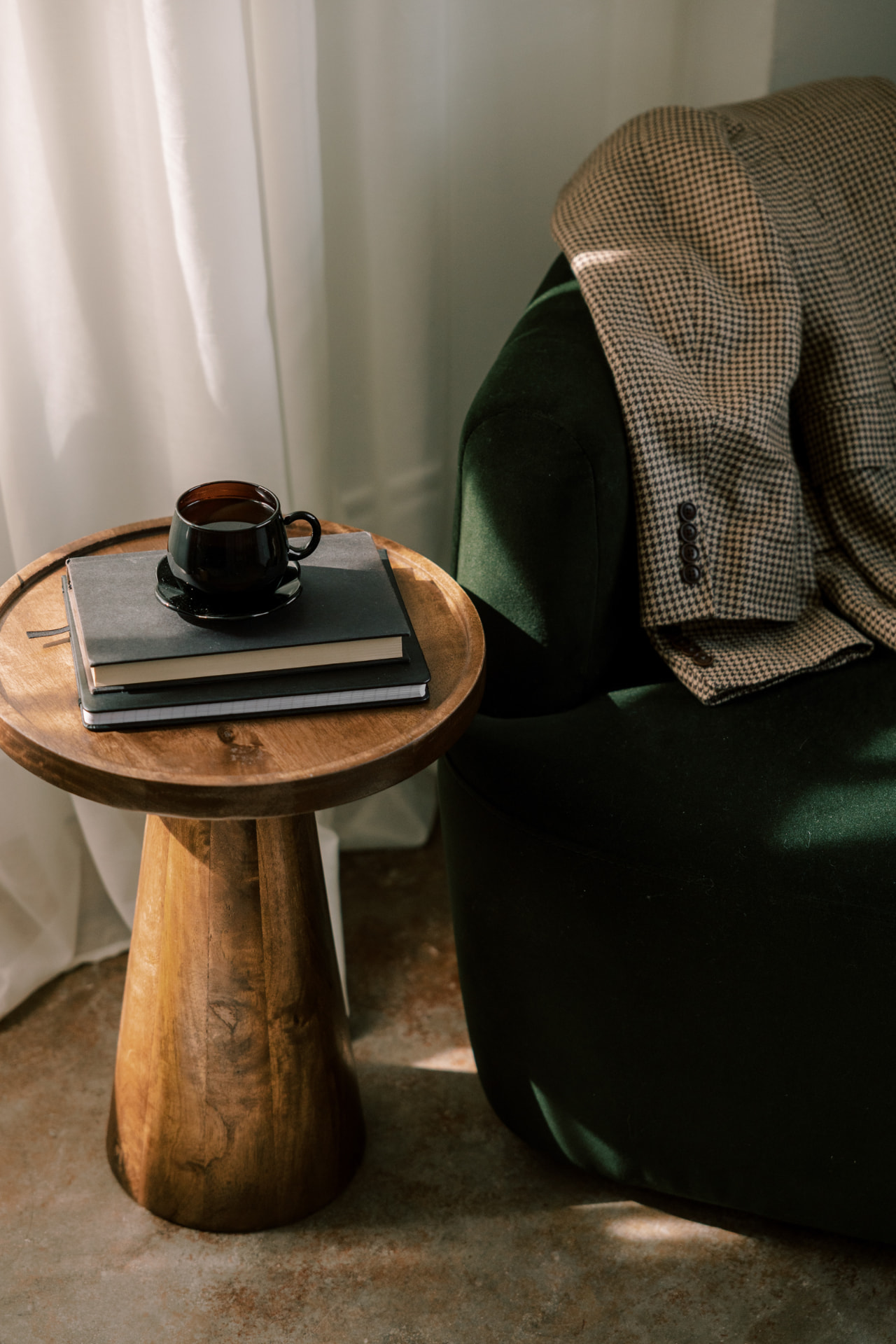 A dark green chair beside a small wooden table with coffee and books.