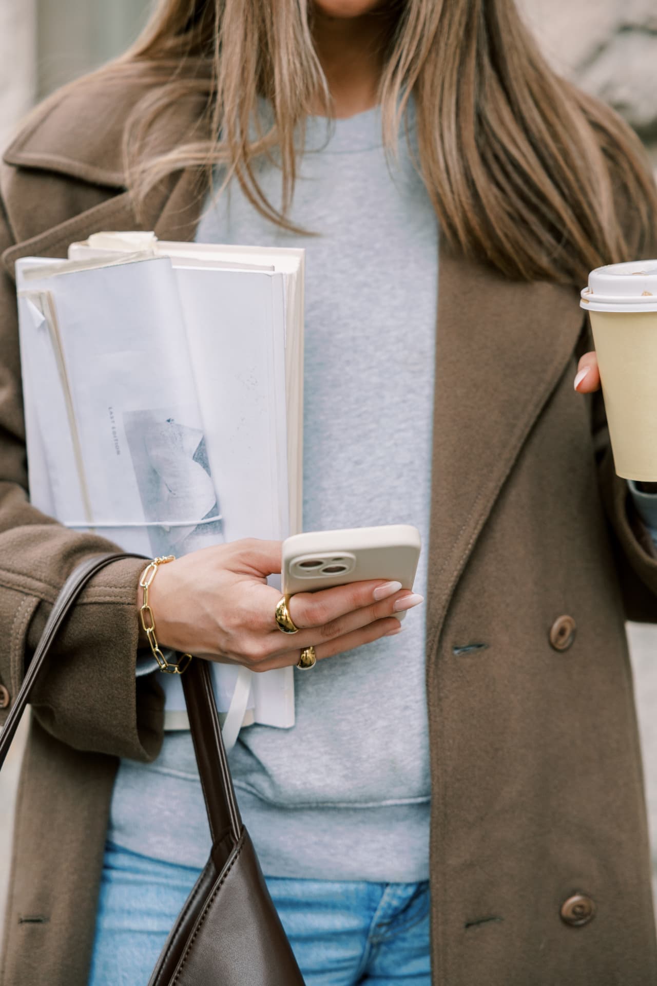 A person holding a phone, papers, and coffee while moving through the day.