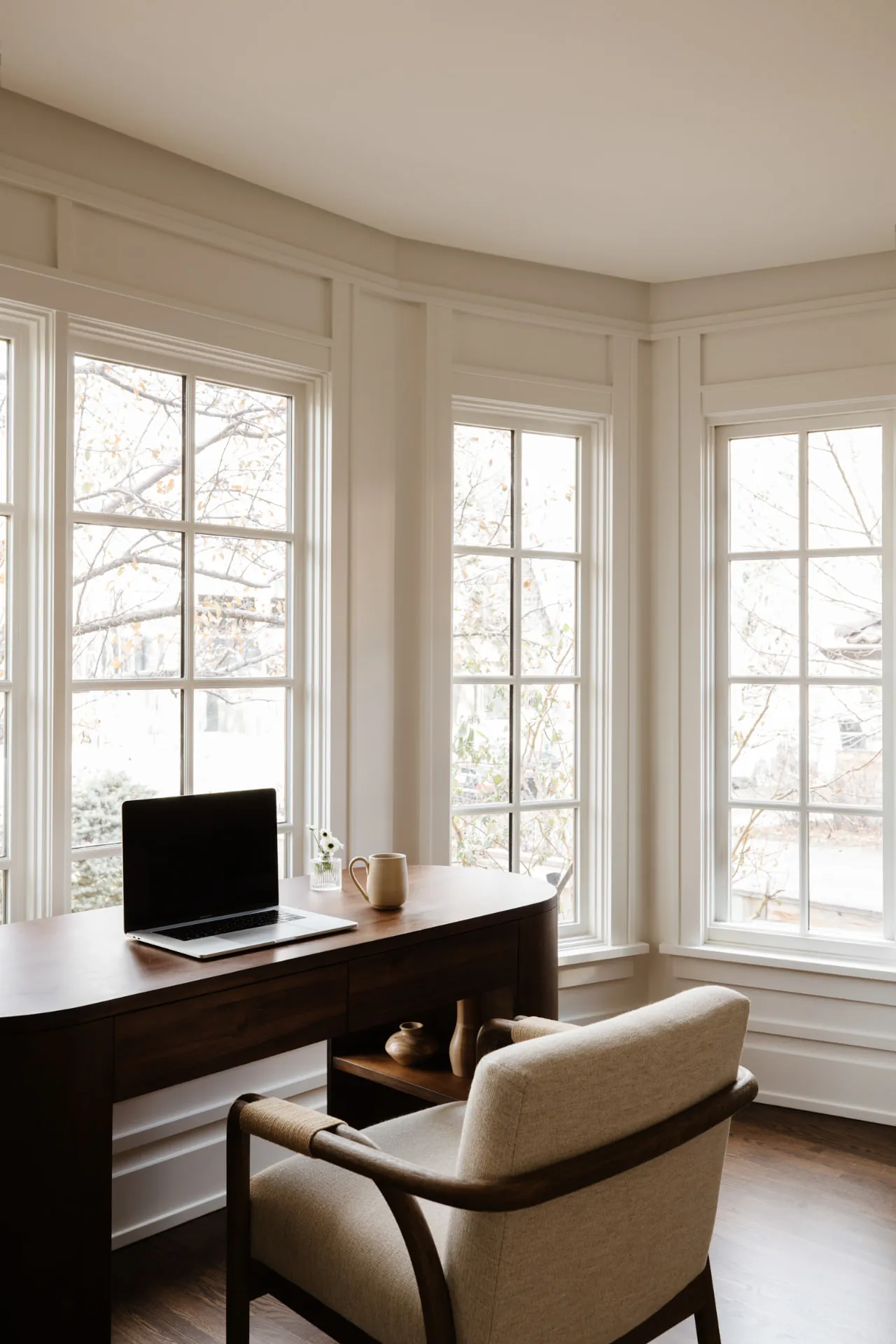A bright bay-window office with a dark wood desk and chair.
