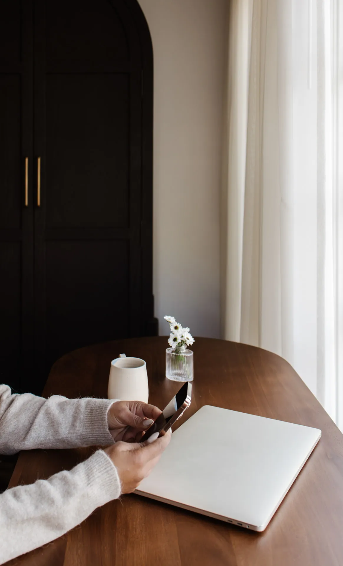 A phone, notebook, and laptop on a wooden desk.