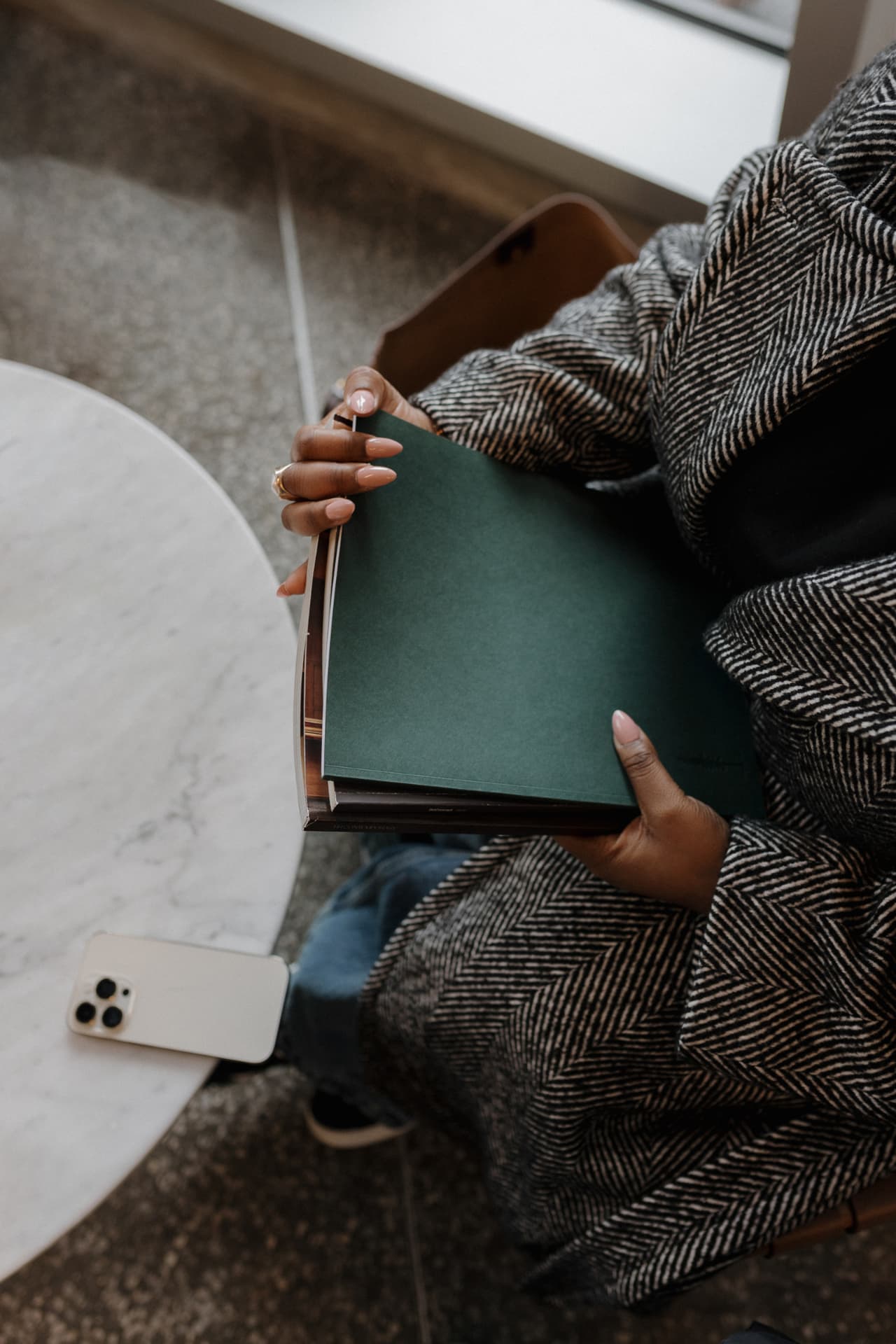 A person holding a green notebook beside a marble table.